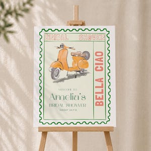 May include: A rectangular sign featuring a postage stamp border in green, displaying an orange scooter illustration. Text reads: BRIDAL SHOWER, BELLA CIAO, WELCOME TO Amelia's BRIDAL SHOWER, and SUNDAY JULY 23. The design is printed on a light cream background.