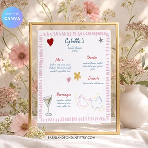 Puede incluir: Un menú de despedida de soltera enmarcado con el nombre "Cybella's" en escritura elegante. El menú presenta ilustraciones de acuarela de corazones, flores y palomas, con elementos como "ternera en salsa de vino tinto" y "panna cotta con bayas". El marco es dorado.