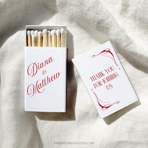 Op de afbeelding: Witte luciferdoos met rode tekst "Diana & Matthew" en "Thank You For Joining Us." De doos is open en toont houten lucifers met witte uiteinden. Het ontwerp is elegant en geschikt voor bruiloften of speciale evenementen.
