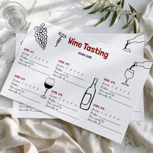 May include: Two white wine tasting score cards with black line drawings of grapes, a corkscrew, wine glasses, and bottles. The red text reads "Wine Tasting Score Card". Each card has spaces to score and describe six wines.