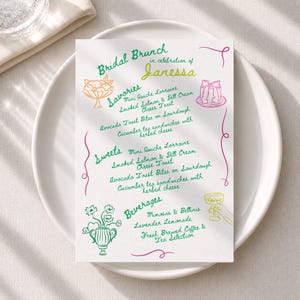 May include: A white rectangular menu card titled Bridal Brunch in celebration of Janessa, featuring green, pink, and yellow hand-drawn illustrations of food, drinks, and flowers, with text listing savory items, sweets, and beverage selections.