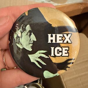 May include: Round button with a black background featuring a green-toned profile of a person and a green hand. The words "HEX ICE" are in white block letters.