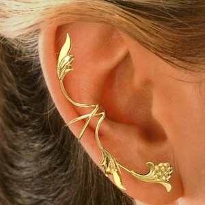 May include: Gold ear cuff with a leaf and flower design. The cuff wraps around the ear and has a delicate, intricate design.