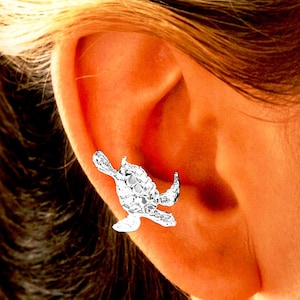 May include: A silver turtle ear cuff earring. The turtle is detailed with a textured shell and is positioned on the upper part of the ear.