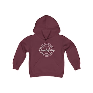Pode incluir: Camisola de capuz cor vinho com um logotipo circular branco que diz "Foundations" e lista matérias como inglês, matemática, latim, ciências, geografia, artes finas e linha do tempo.