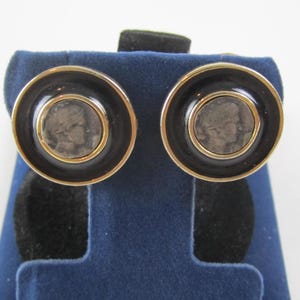 May include: A pair of gold-tone earrings with black enamel and a silver coin design. The coins feature a profile of a person's face.