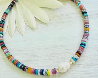 May include: A colorful beaded necklace with a large white pearl pendant. The necklace features a variety of small, flat beads in shades of blue, pink, yellow, and orange. The clasp is gold-colored.