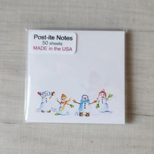 May include: A pack of 50 Post-it® Notes with a winter theme featuring four snowmen with colorful hats and scarves. The pack is labeled "Post-it® Notes 50 sheets MADE in the USA."