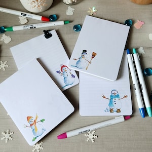 May include: Four white lined notebooks with different snowman illustrations. Each notebook has a snowman with a different hat and scarf. The snowmen are drawn in watercolor.