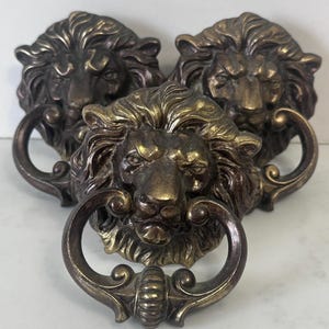 May include: Three antique bronze lion head door knockers. Each lion head has detailed manes and a ring-shaped knocker. The bronze finish gives the knockers a vintage look, suitable for adding a touch of classic elegance to any door.