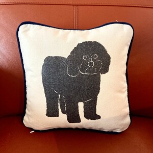 May include: A white pillow with a black silhouette of a dog on it. The pillow has a navy blue trim.