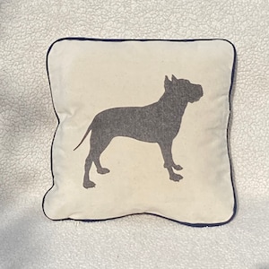 May include: A white throw pillow with a navy blue border features a black silhouette of a dog.