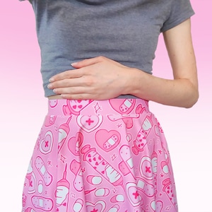 Pode incluir: Uma saia rosa com estampa branca e rosa de cora&ccedil;&otilde;es, bandagens e seringas. A saia &eacute; plissada e tem uma silhueta evas&ecirc;.