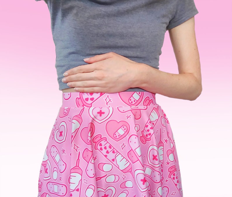 Pode incluir: Uma saia rosa com estampa branca e rosa de cora&ccedil;&otilde;es, bandagens e seringas. A saia &eacute; plissada e tem uma silhueta evas&ecirc;.