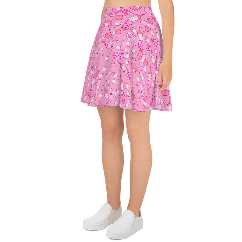 Pode incluir: Uma saia skater rosa com um padr&atilde;o de bandagens, p&iacute;lulas e seringas rosa e brancas.
