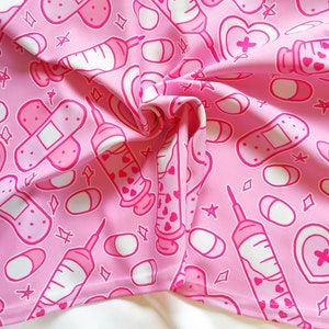 Pode incluir: Tecido rosa com um padr&atilde;o repetido de bandagens brancas, seringas e p&iacute;lulas. O padr&atilde;o &eacute; em um estilo de desenho animado bonito.
