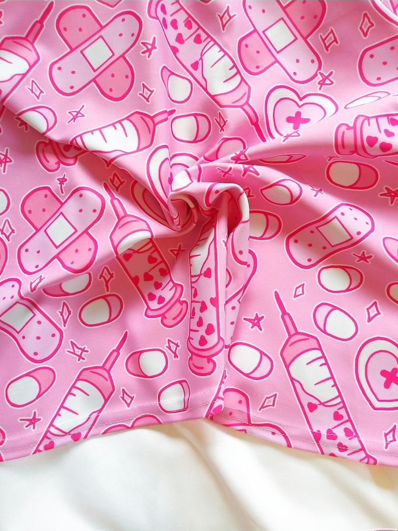 Pode incluir: Tecido rosa com um padr&atilde;o repetido de bandagens brancas, seringas e p&iacute;lulas. O padr&atilde;o &eacute; em um estilo de desenho animado bonito.