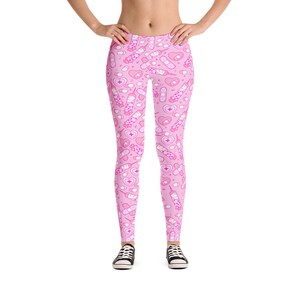 May include: Pink leggings with a repeating pattern of medical-themed illustrations, including syringes, bandages, pills, and hearts. The leggings are worn with black sneakers.