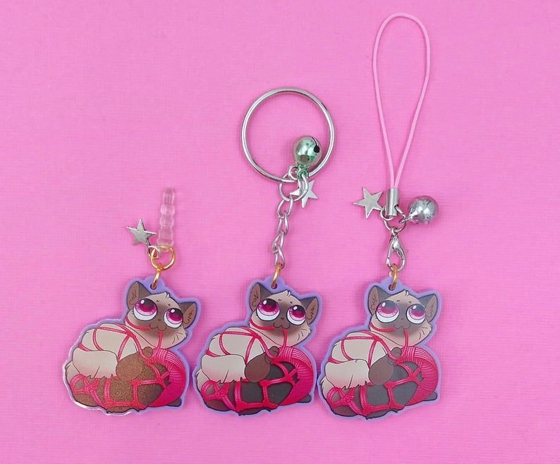 May include: Three pink and white cat charms with pink string and silver star charms. Each charm is attached to a silver chain with a silver ring.
