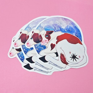 Peut inclure: Trois autocollants empil&eacute;s repr&eacute;sentant une vache de dessin anim&eacute; avec des marques brunes et blanches, couch&eacute;e sur un fond aquarelle bleu et violet avec des &eacute;toiles. La vache a un patch en forme de c&oelig;ur sur le c&ocirc;t&eacute; et une &eacute;toile noire sur l'arri&egrave;re-train. Les autocollants portent le texte "@frostedsosweet" imprim&eacute; dessus.