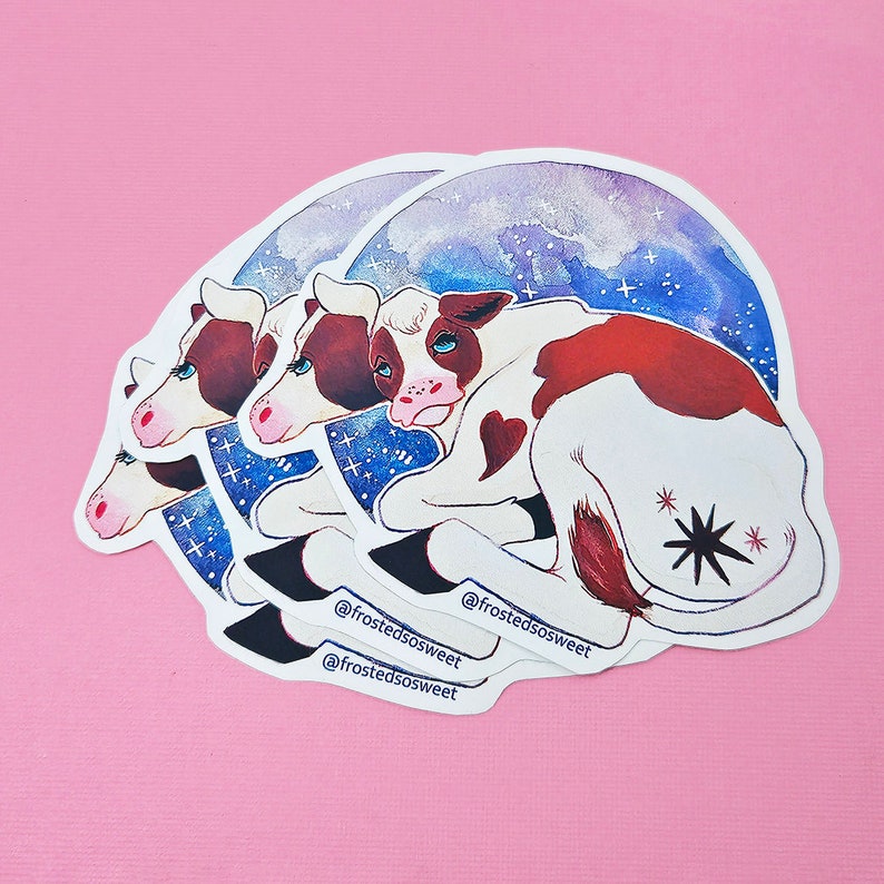 Peut inclure: Trois autocollants empil&eacute;s repr&eacute;sentant une vache de dessin anim&eacute; avec des marques brunes et blanches, couch&eacute;e sur un fond aquarelle bleu et violet avec des &eacute;toiles. La vache a un patch en forme de c&oelig;ur sur le c&ocirc;t&eacute; et une &eacute;toile noire sur l'arri&egrave;re-train. Les autocollants portent le texte "@frostedsosweet" imprim&eacute; dessus.