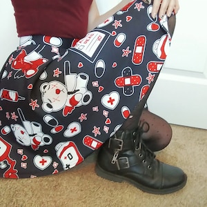May include: A black skirt with a white and red print of teddy bears, bandages, hearts, and pills. The skirt has a pleated design and is worn with black tights and black combat boots.