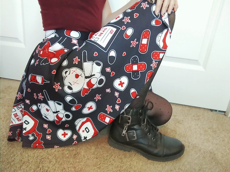 May include: A black skirt with a white and red print of teddy bears, bandages, hearts, and pills. The skirt has a pleated design and is worn with black tights and black combat boots.