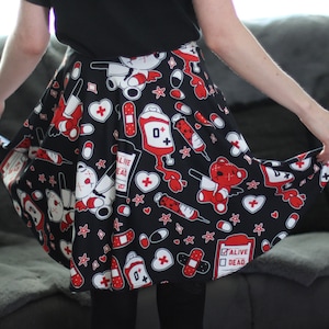 May include: A black skirt with a red and white print of teddy bears, bandages, hearts, pills, and syringes. The skirt has a flared silhouette and is made of a soft, stretchy fabric.