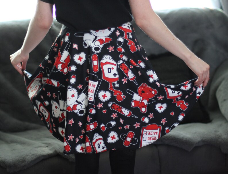 May include: A black skirt with a red and white print of teddy bears, bandages, hearts, pills, and syringes. The skirt has a flared silhouette and is made of a soft, stretchy fabric.