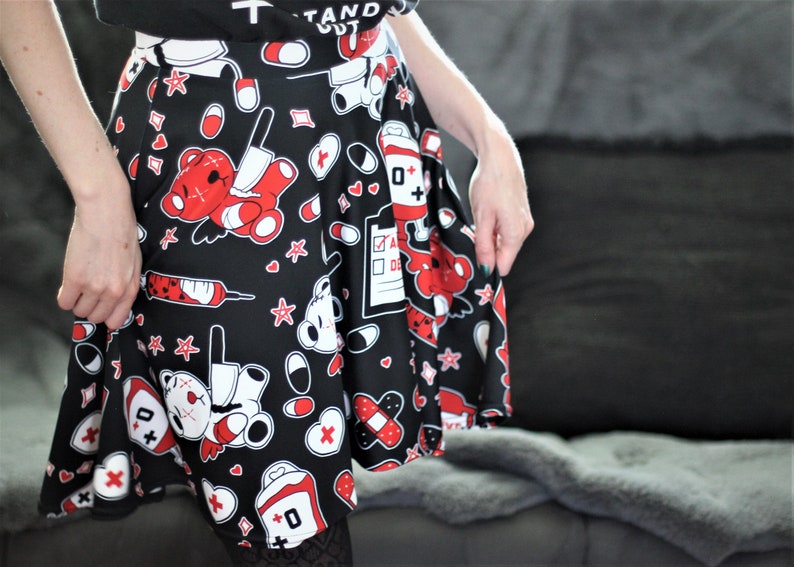 May include: A black skater skirt with a red and white print of cartoon teddy bears, bandages, pills, and hearts. The skirt has a pleated design and is made of a soft, stretchy fabric.