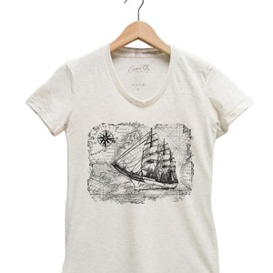 Puede incluir: Una camiseta blanca de cuello en V con un estampado gr&aacute;fico en blanco y negro de un barco navegando en un mapa vintage con una br&uacute;jula.