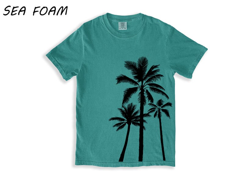 K&ouml;nnte beinhalten: Meergr&uuml;nes T-Shirt mit schwarzem Palmen-Motiv. Das T-Shirt hat einen Rundhalsausschnitt und kurze &Auml;rmel. Der Text "SEA FOAM" befindet sich in der oberen linken Ecke. Die Grafik zeigt drei unterschiedlich hohe Palmen.