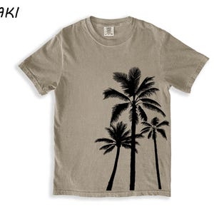 K&ouml;nnte beinhalten: Khaki-farbenes T-Shirt mit einer schwarzen Silhouette von drei Palmen. Das Shirt hat einen Rundhalsausschnitt und kurze &Auml;rmel. Das Wort "KHAKI" ist oben links in Schwarz aufgedruckt.