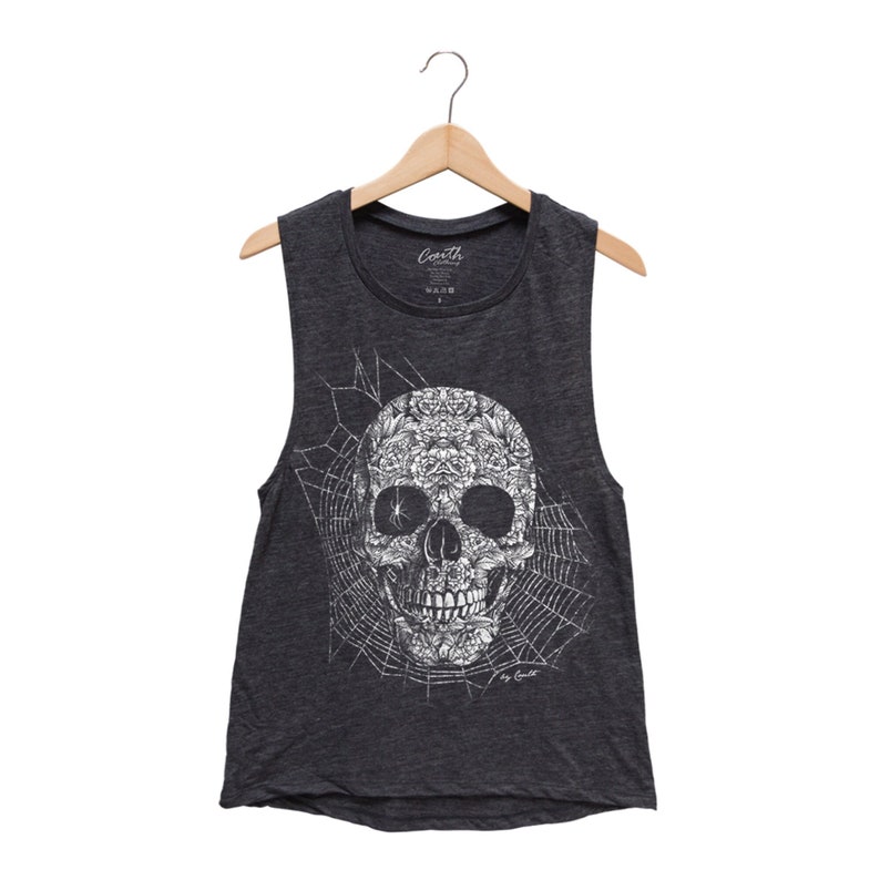 May include: A dark gray sleeveless shirt with a white floral skull design on a spiderweb background. The shirt has a crew neck and a relaxed fit. The text "Carth" is printed on the tag.