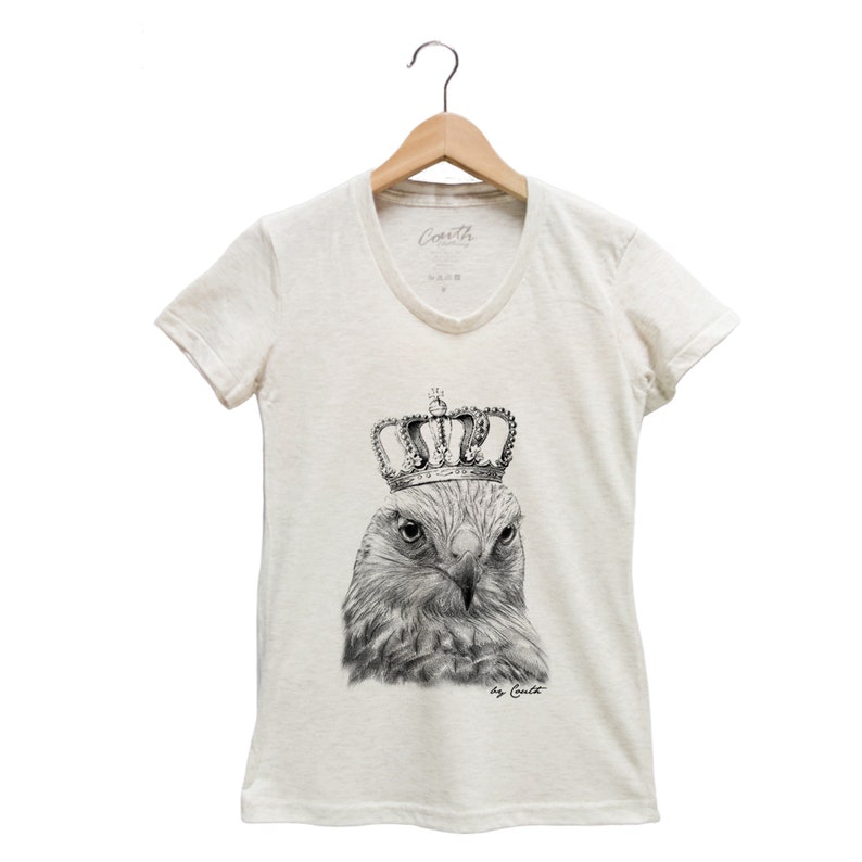 May include: A white t-shirt with a black and white illustration of a hawk wearing a gold crown. The text "by Coult" is printed below the illustration.