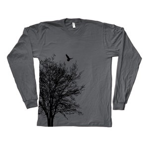 May include: A charcoal grey long-sleeved t-shirt featuring a black silhouette of a tree and a bird flying above it. The design is on the left side of the shirt.