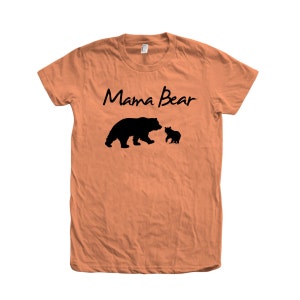 May include: A peach-colored t-shirt with the text "Mama Bear" in black script. A black silhouette of a mama bear and a cub are below the text.