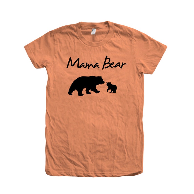 May include: A peach-colored t-shirt with the text "Mama Bear" in black script. A black silhouette of a mama bear and a cub are below the text.