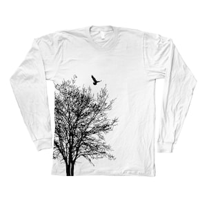 May include: White long-sleeved t-shirt featuring a black silhouette of a tree and a bird in flight above it.