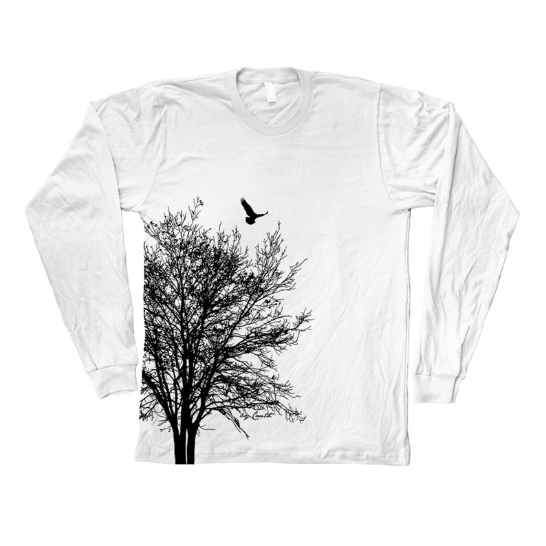May include: White long-sleeved t-shirt featuring a black silhouette of a tree and a bird in flight above it.