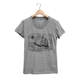 Puede incluir: Camiseta gris con una ilustraci&oacute;n vintage de un barco navegando en un mapa con una br&uacute;jula.