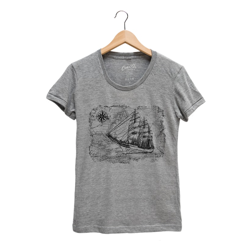 Puede incluir: Camiseta gris con una ilustraci&oacute;n vintage de un barco navegando en un mapa con una br&uacute;jula.