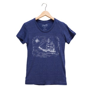 Puede incluir: Una camiseta azul marino con un gr&aacute;fico blanco de un barco navegando en un mapa con una br&uacute;jula. El texto "South Clothing" es visible en la camiseta.