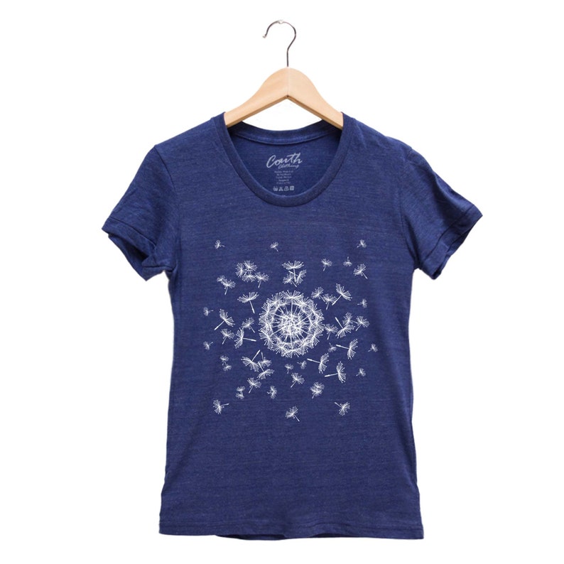 May include: A navy blue t-shirt with a white graphic of a dandelion blowing seeds. The shirt has a crew neck and short sleeves.