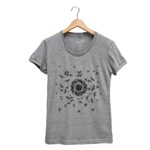 May include: A heather grey t-shirt with a black dandelion design. The dandelion is in the center of the shirt and has seeds blowing in the wind.