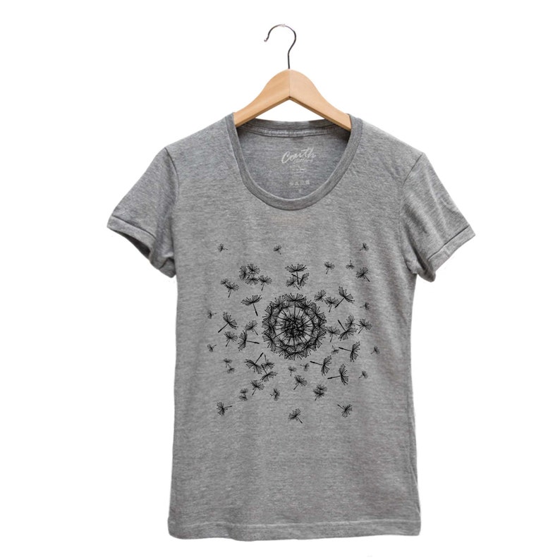 May include: A heather grey t-shirt with a black dandelion design. The dandelion is in the center of the shirt and has seeds blowing in the wind.