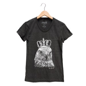 May include: A charcoal gray t-shirt with a black and white illustration of a hawk wearing a crown. The text "by Coult" is printed below the image.