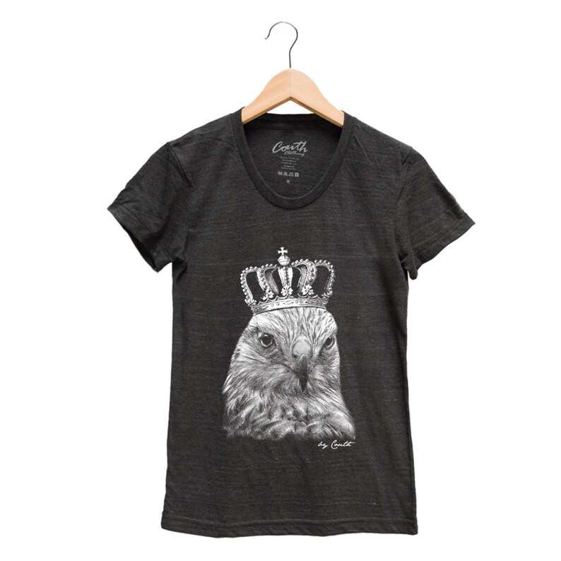 May include: A charcoal gray t-shirt with a black and white illustration of a hawk wearing a crown. The text "by Coult" is printed below the image.
