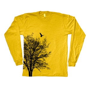 May include: A yellow long-sleeved t-shirt featuring a black silhouette of a tree and a bird flying above it. The shirt has a distressed look and the design is on the left side of the shirt.