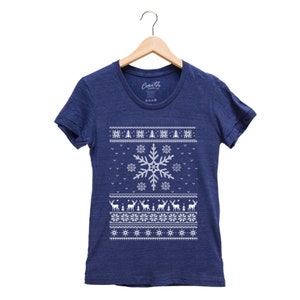 May include: A navy blue t-shirt with a white snowflake and reindeer pattern. The shirt has a crew neck and short sleeves.